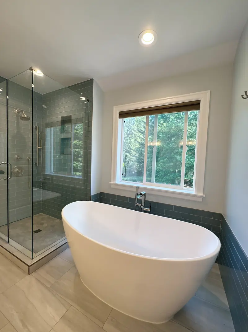 Freestanding tub beside a frameless glass shower lined in blue glass subway tile