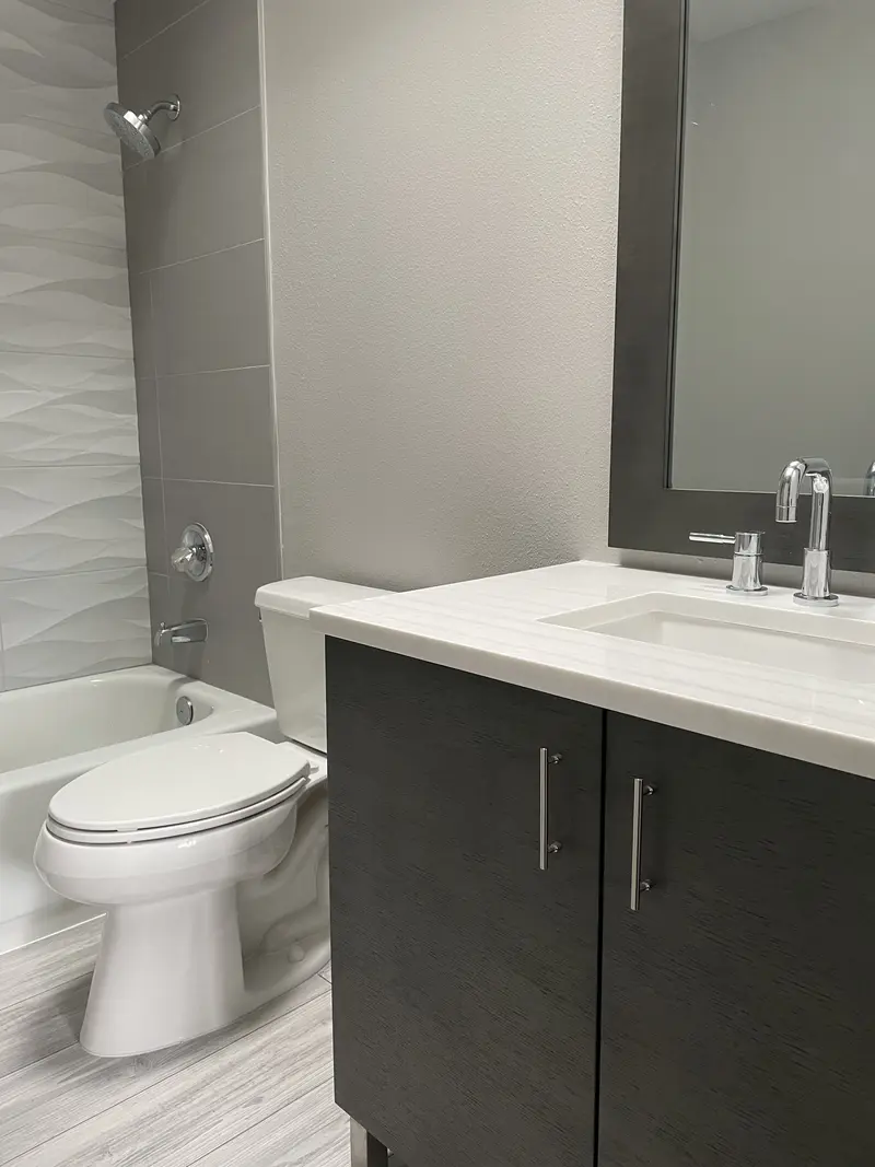 Espresso flat-panel vanity with a white top, chrome faucet and a toilet beside it on plank tile
