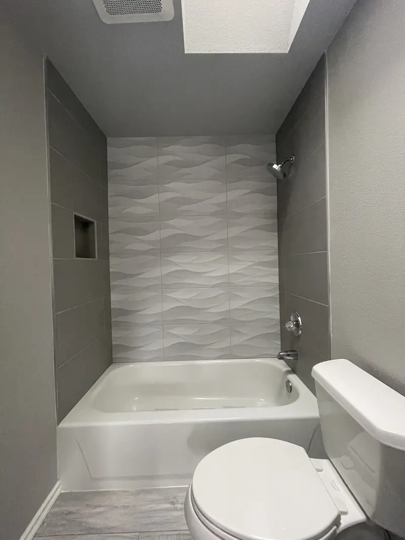 Tub and shower under a skylight, seen past the toilet, with wave tile on the back wall