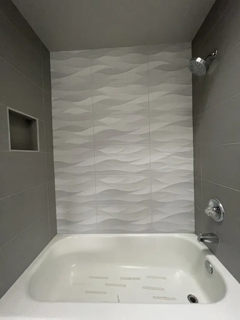 White tub with a chrome shower head, valve and spout against the white wave tile