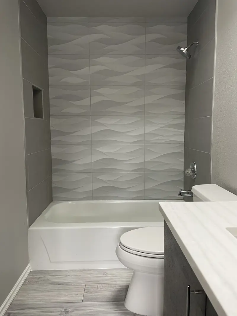 Tub and shower with a white sculpted wave tile back wall and smooth gray tile side walls