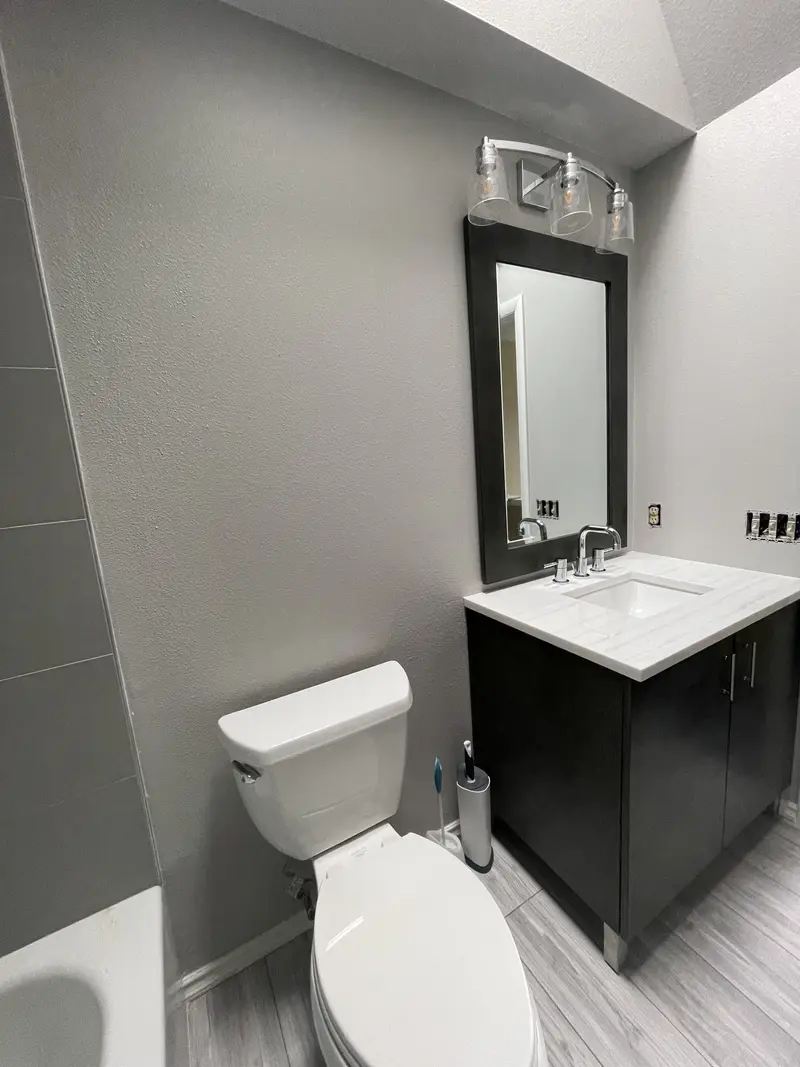 Vanity, mirror and toilet along a wall under a sloped ceiling with a three-light fixture