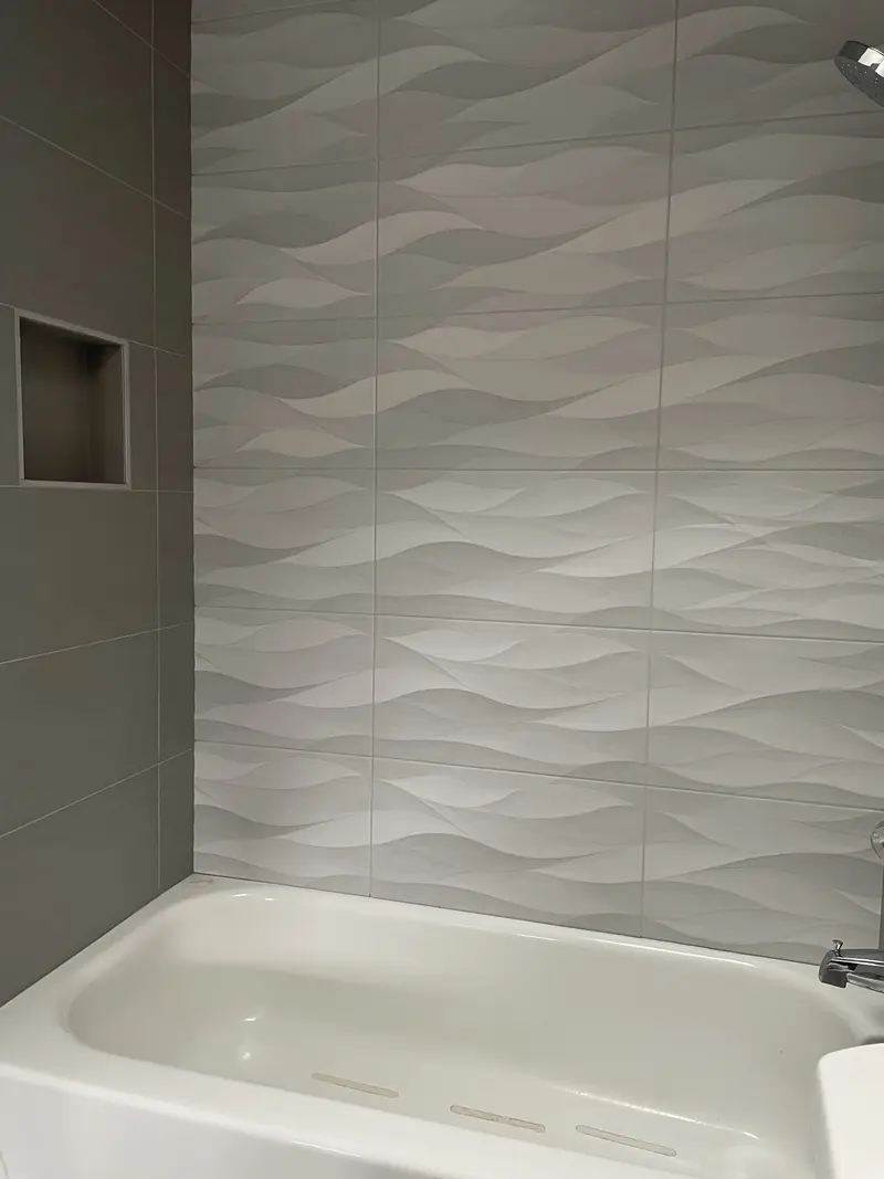 White wave tile shower wall with a recessed niche in the gray side wall above a white tub
