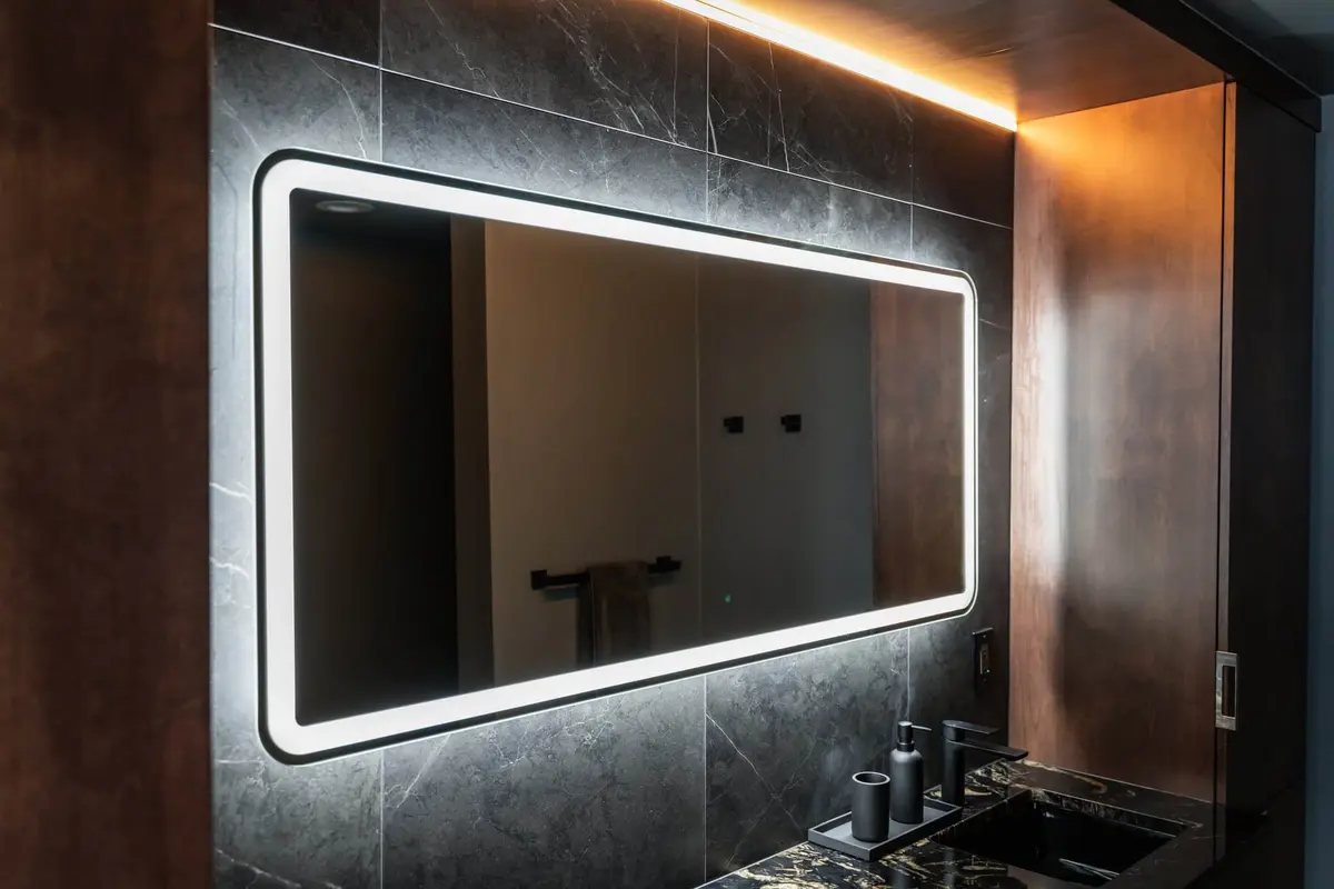 Backlit mirror on a black marble-look tile wall between warm wood panels