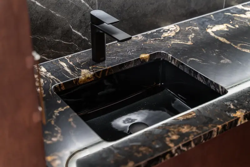 Black sink set in a black and gold veined stone-look counter with a matte black faucet