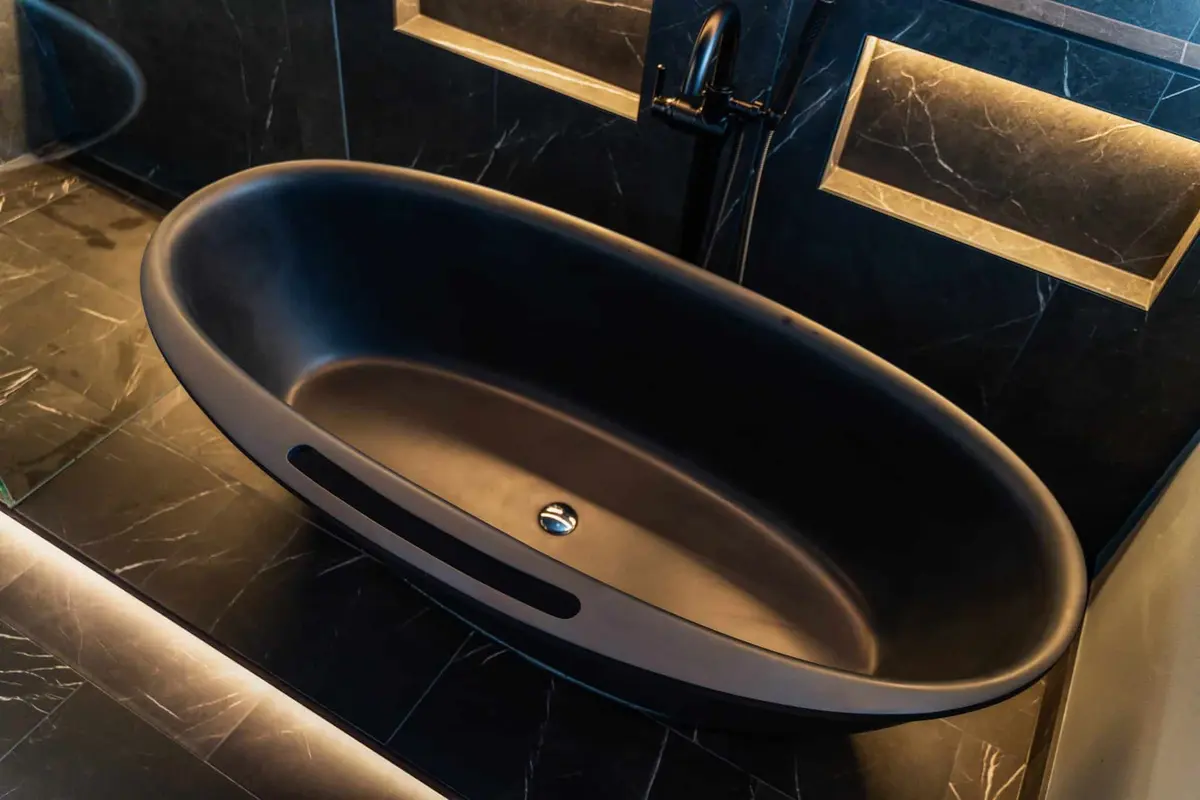 Black oval freestanding tub on black marble-look floor tile in a basement bathroom