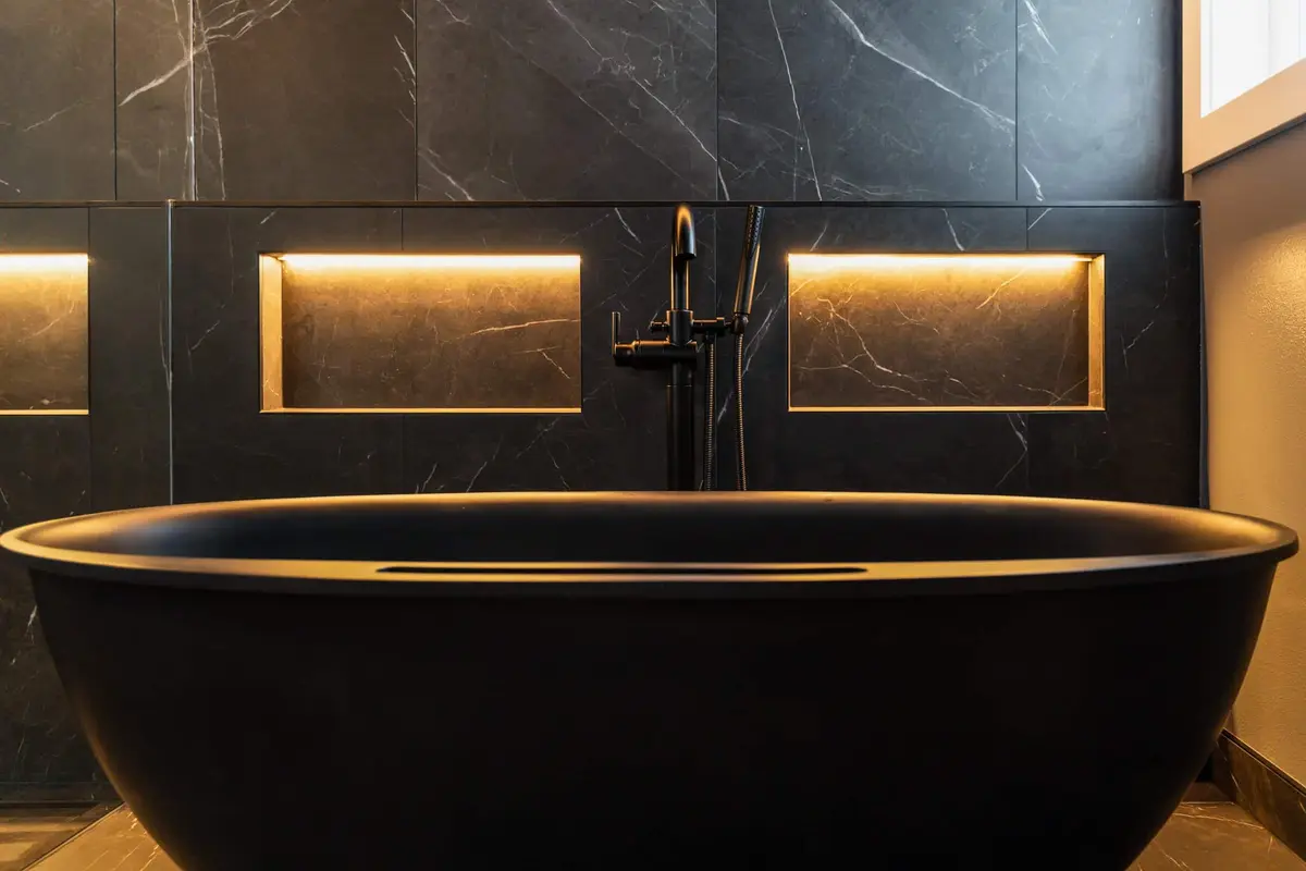 Black freestanding tub with a matte black floor-mounted faucet and lit wall niches