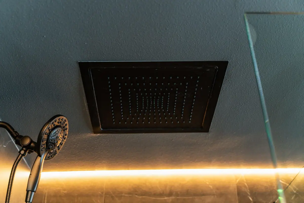 Square ceiling rain shower panel above a matte black handheld shower and dark walls