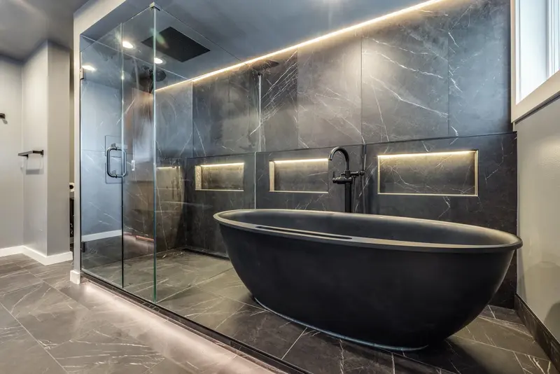 Glass-enclosed wet area holding the black tub and the shower, seen from the vanity side
