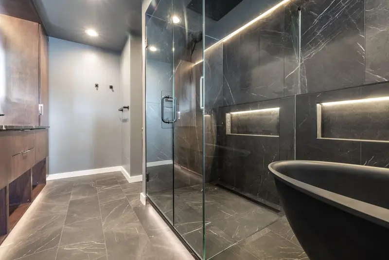 View from the doorway into the glass-enclosed wet area with the black tub and lit niches