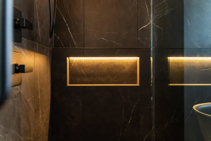 Recessed niche with warm LED light set into a black marble-look shower wall