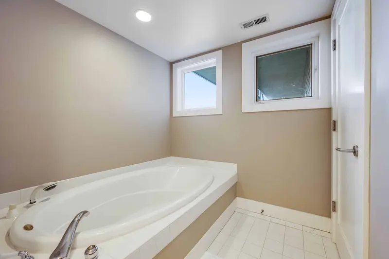 Old white corner tub under two small windows with beige walls
