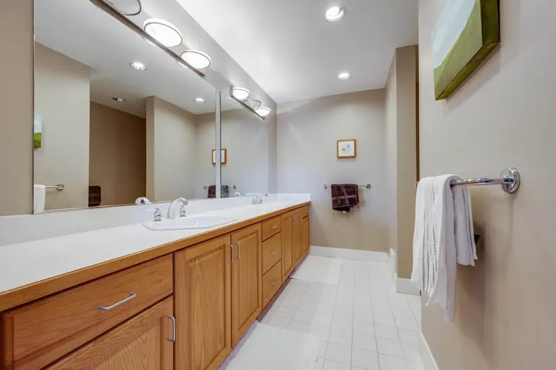 Bathroom before the remodel with a long light wood double vanity, white counter and a wide mirror
