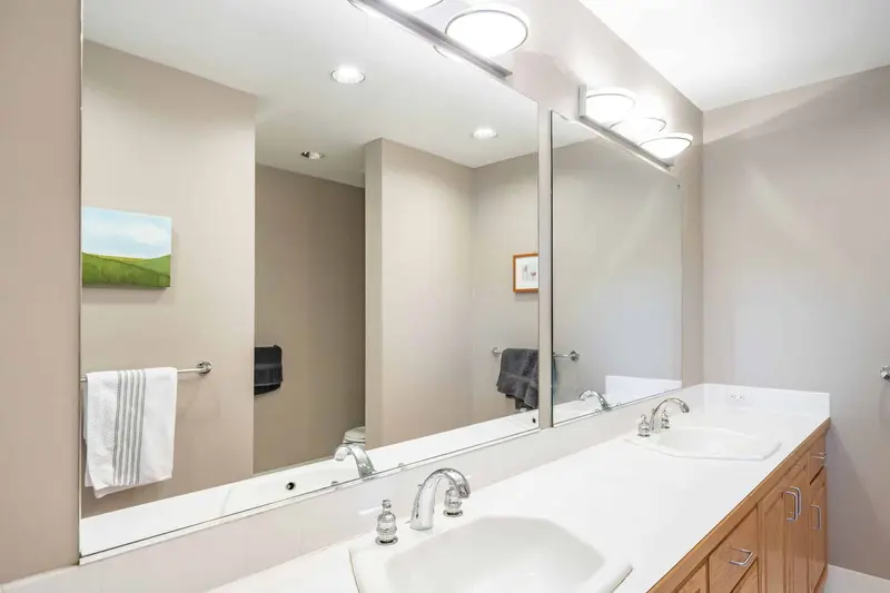 Old white vanity counter with two sinks, a wide mirror and globe lights