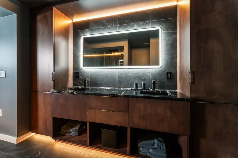 Wood vanity with an open lower shelf and warm LED light along its toe kick