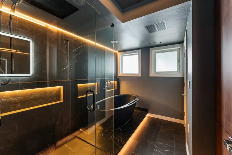 Glass wet area under two windows with a warm LED cove along the ceiling