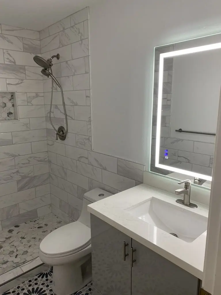 Gray vanity with a white top under a backlit LED mirror, next to the toilet and the shower