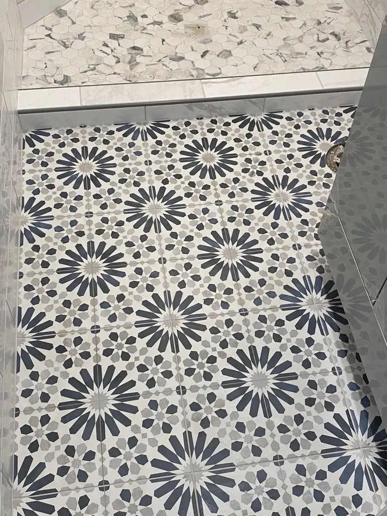 Navy and white star pattern floor tile meeting the pebble shower floor at a marble-look curb