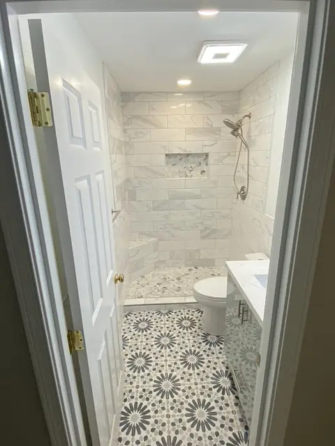 View through the bathroom door to a marble-look tile walk-in shower over a navy and white patterned floor