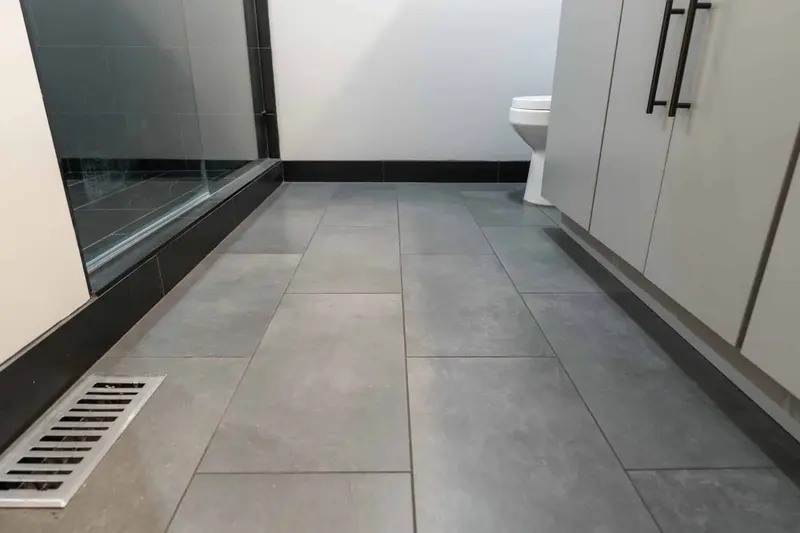 Gray large tile bathroom floor running past the frameless glass shower wall and tall cabinet