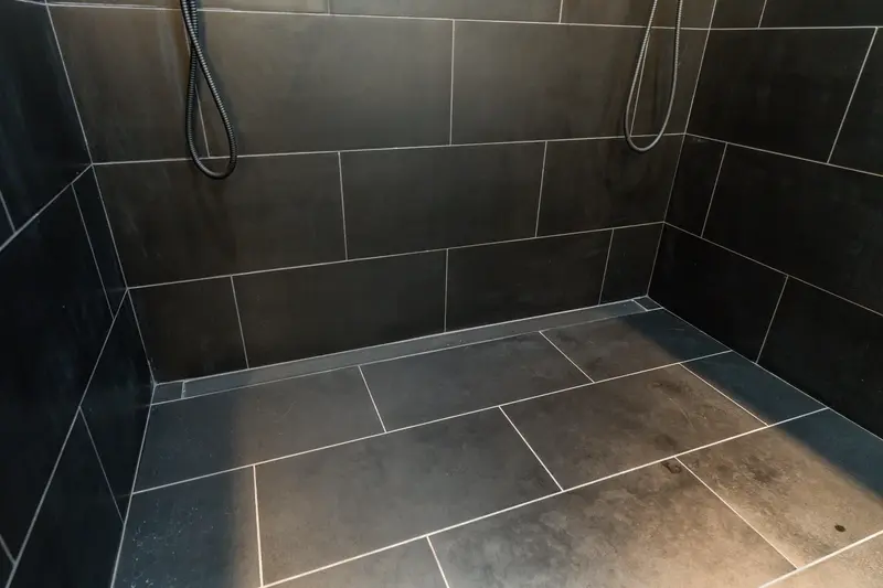 Shower floor in charcoal tile with a linear drain along the wall and a hand shower on a slide bar
