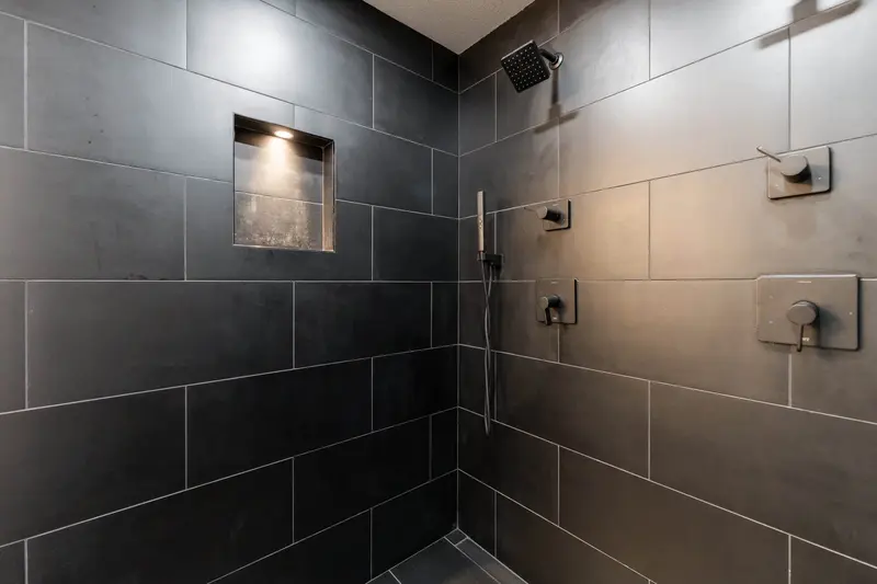 Charcoal tile shower wall with a lit recessed niche and matte black controls