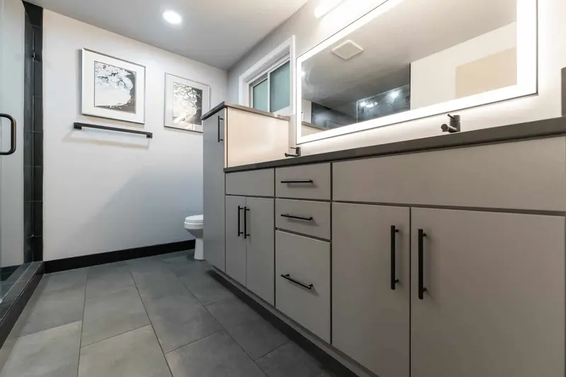 Gray flat-panel vanity drawers and doors with black pulls beside the glass shower wall