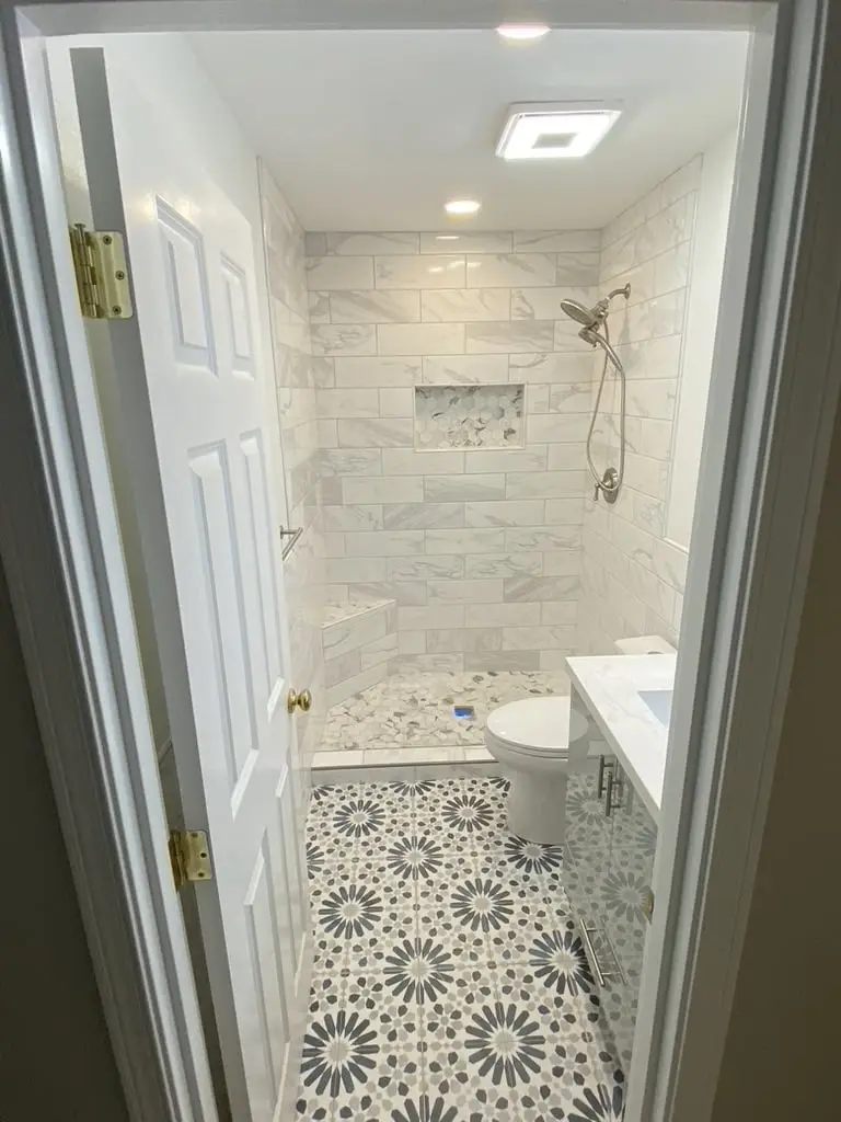 View through the bathroom door to a marble-look tile walk-in shower over a navy and white patterned floor