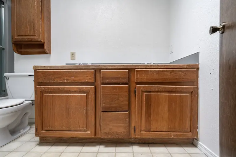 Oak vanity and toilet on a beige vinyl floor before the remodel