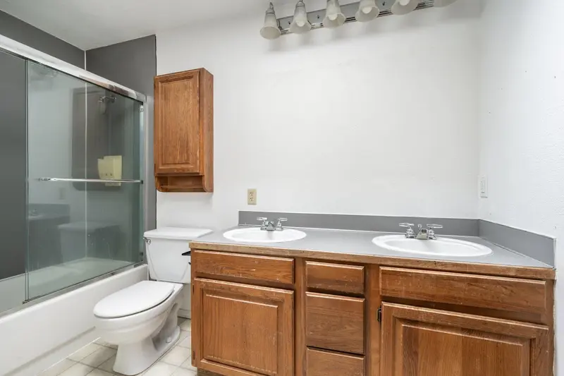Old tub with framed sliding doors beside an oak vanity and a wall cabinet