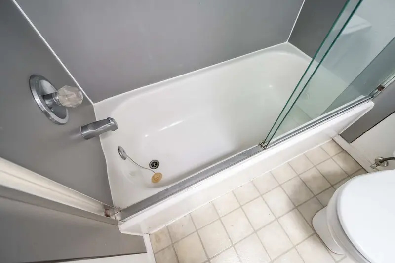 Looking down into the old tub with a gray surround and a beige vinyl floor beside it