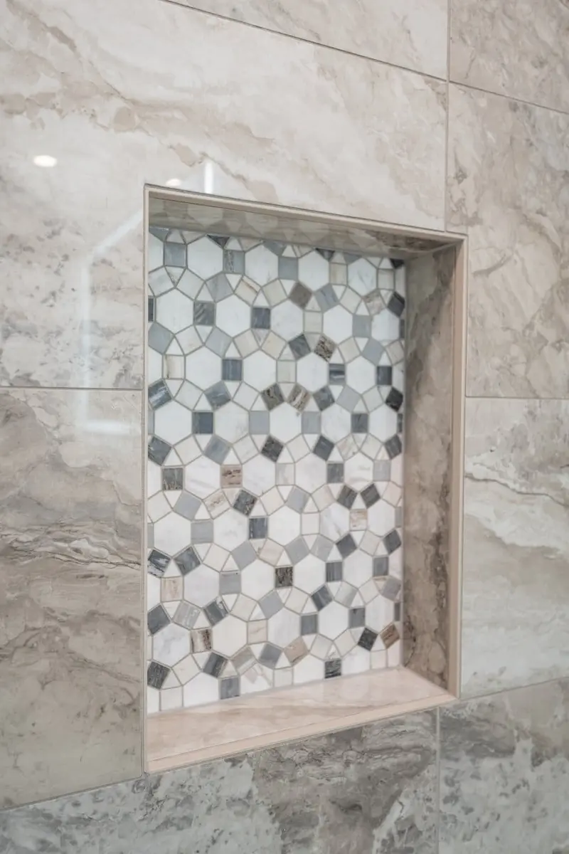 Recessed shower niche lined with a gray and white hexagon mosaic in marble-look wall tile