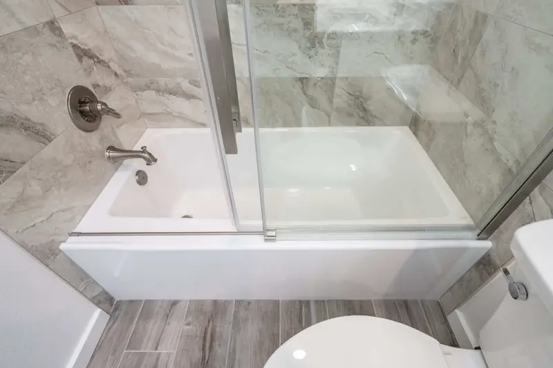 New white tub behind a glass slider, above a wood-look plank floor