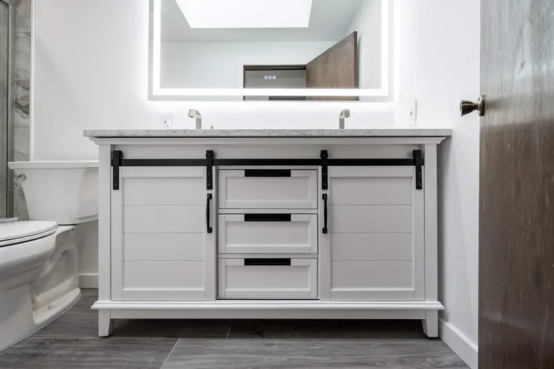 White vanity with two sinks under a wide backlit mirror and a skylight reflection