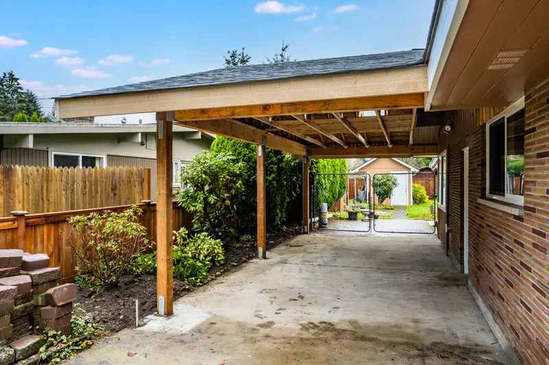 Open end of the new carport with wood posts, trusses and shingle roof, looking down the side yard