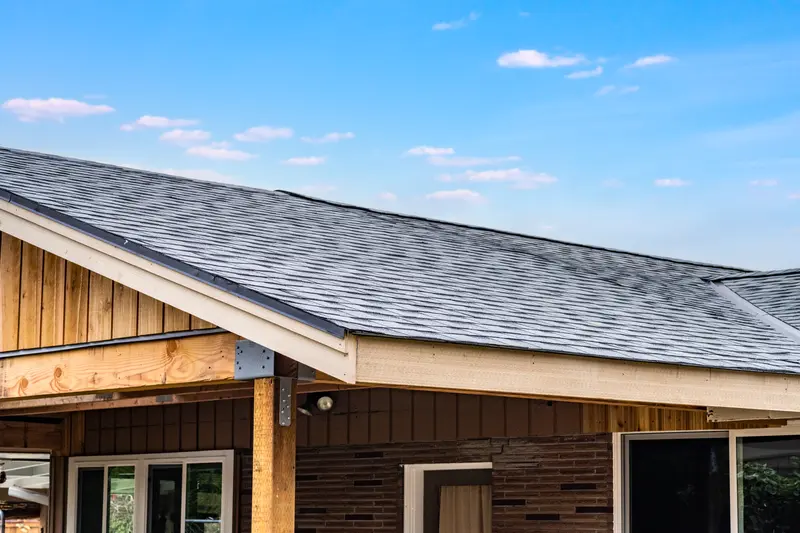New asphalt shingle roof edge and white trim on the carport against a blue sky