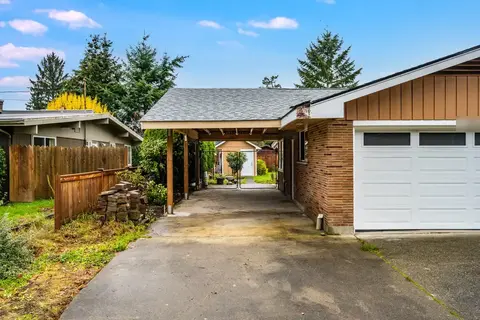New gable roof carport running along the side of a brick house beside a white garage door