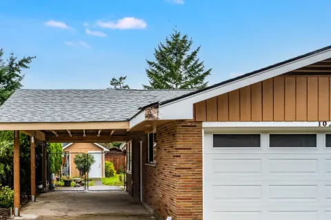New gable roof carport running along the side of a brick house beside a white garage door