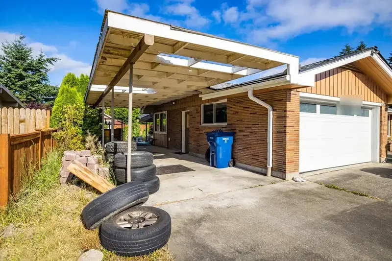 Old carport roof of translucent corrugated panels on a white frame, beside the garage door