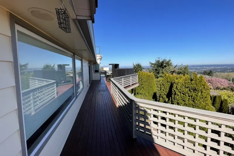 Refinished wood deck with a white lattice railing along a house, overlooking evergreens, from a Bellevue deck project by Volcano Builders