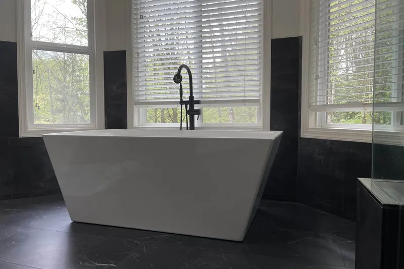 Freestanding soaking tub with a black floor-mounted filler under three windows, from an Issaquah bathroom remodel by Volcano Builders
