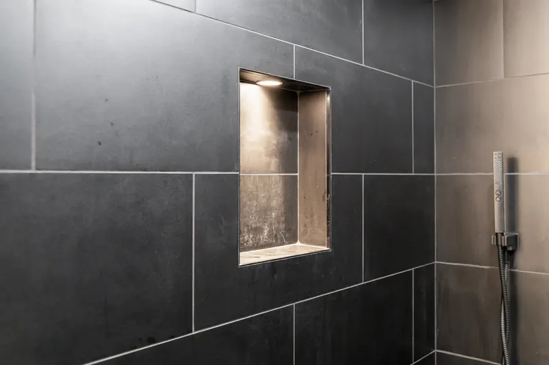 Walk-in shower in large-format charcoal tile with a lit recessed niche and a matte black hand shower, from a Kirkland bathroom remodel by Volcano Builders