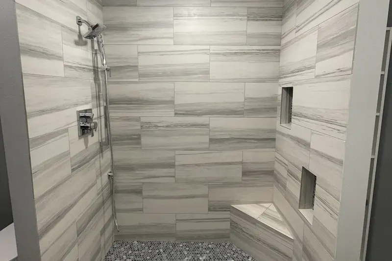 Walk-in shower with grey plank tile, a corner bench, two niches and a pebble mosaic floor, from a Federal Way basement remodel by Volcano Builders