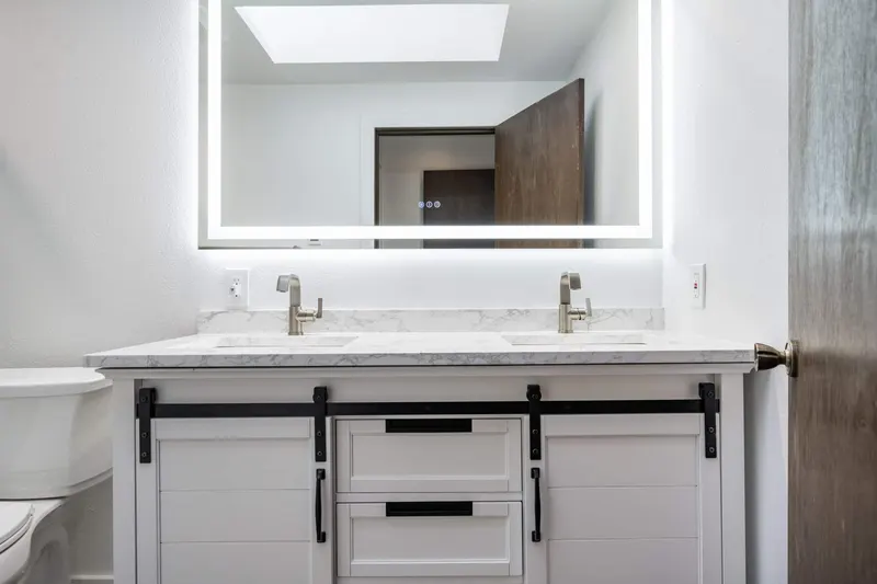 White double vanity with sliding barn doors, a marble look top and a backlit mirror, from a Tulalip Bay bathroom remodel by Volcano Builders