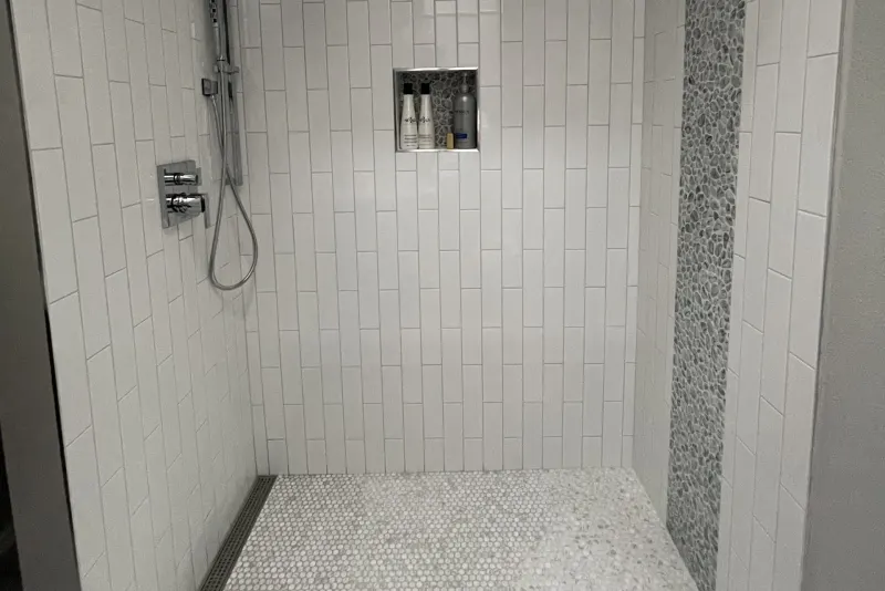 Walk-in shower from a Seattle master bathroom remodel, white vertical tile, a pebble accent strip and a wall niche