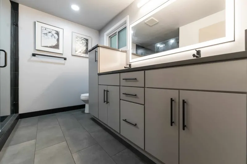 Remodeled bathroom with a long gray vanity, black pulls, a backlit mirror and large gray floor tile, from a Kirkland bathroom renovation by Volcano Builders