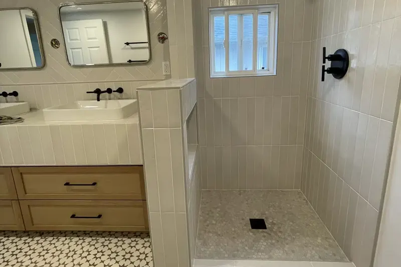 Curbed walk-in shower with stacked vertical tile, a hex tile floor and a window, beside a light oak vanity, from a Seattle bathroom remodel by Volcano Builders