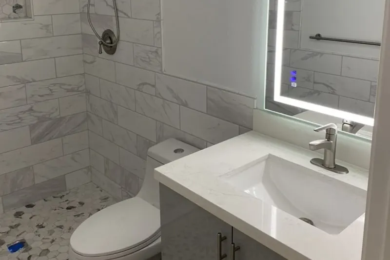 Bathroom with marble look wall tile, a gray vanity with a white top and a lighted mirror, from a Newcastle remodel by Volcano Builders