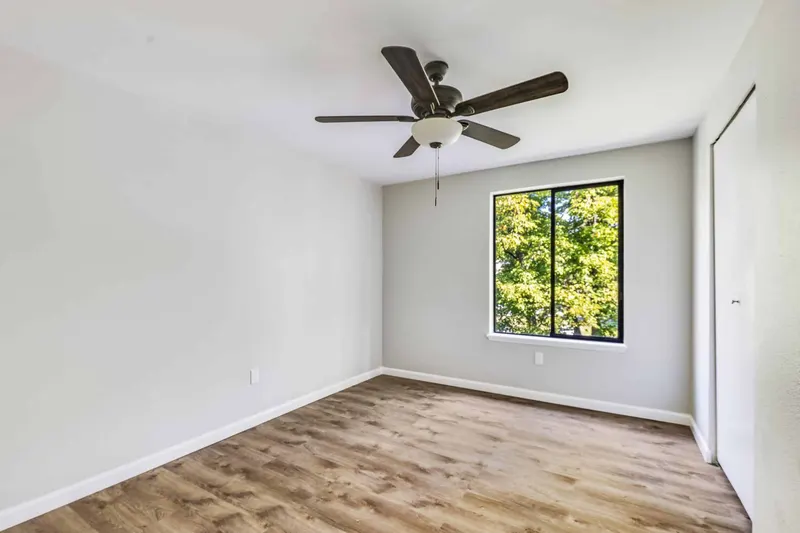 Finished bedroom with new plank flooring, grey walls, a ceiling fan and a black framed window facing trees, from a Renton remodel by Volcano Builders