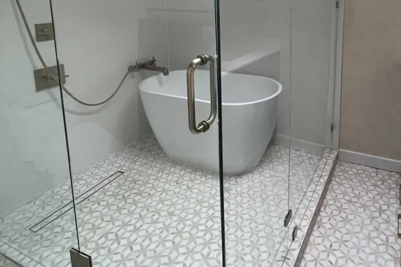 White soaking tub inside a frameless glass wet room with a flower mosaic floor, from a Seattle bathroom remodel by Volcano Builders